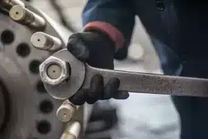Close-up of a gloved hand using a large Ampco non-sparking box end striking wrench on an industrial bolt, demonstrating the application of heavy-duty safety tools in demanding maintenance operations.